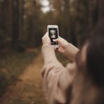 girl holding phone up to take photo in a forest