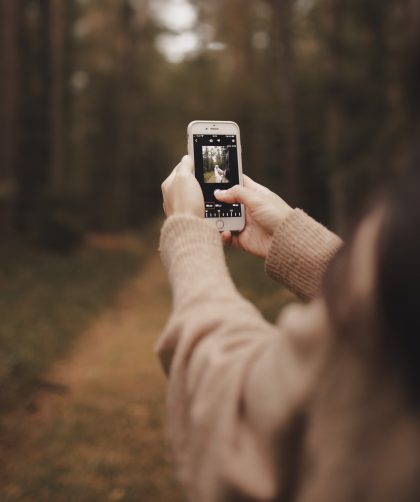 girl holding phone up to take photo in a forest